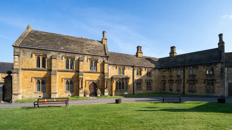 Historic stone almshouses around a lawn in England on a sunny day