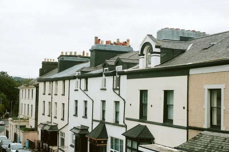 A row of painted terraced houses with bay windows and chimneys on a hillside street